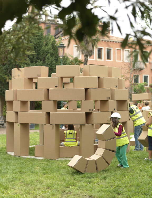 A structure made of cardboard being made by people in high vis