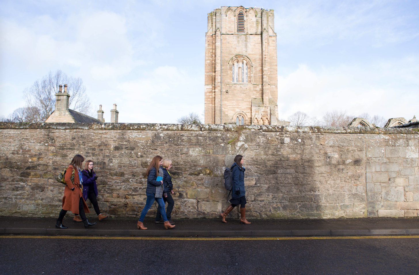 A group of people walk along a stone wall