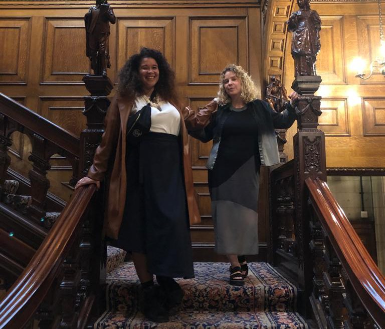 Nicola Jeffs & Alberta Whittle stand on a carpeted staircase.