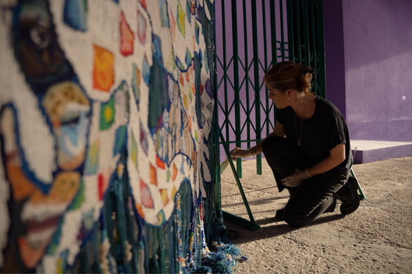 Alice Rose Archer crouches in front of a tapestry created for Alberta Whittle's 2022 exhibition in Venice - Image by Joe Satorius